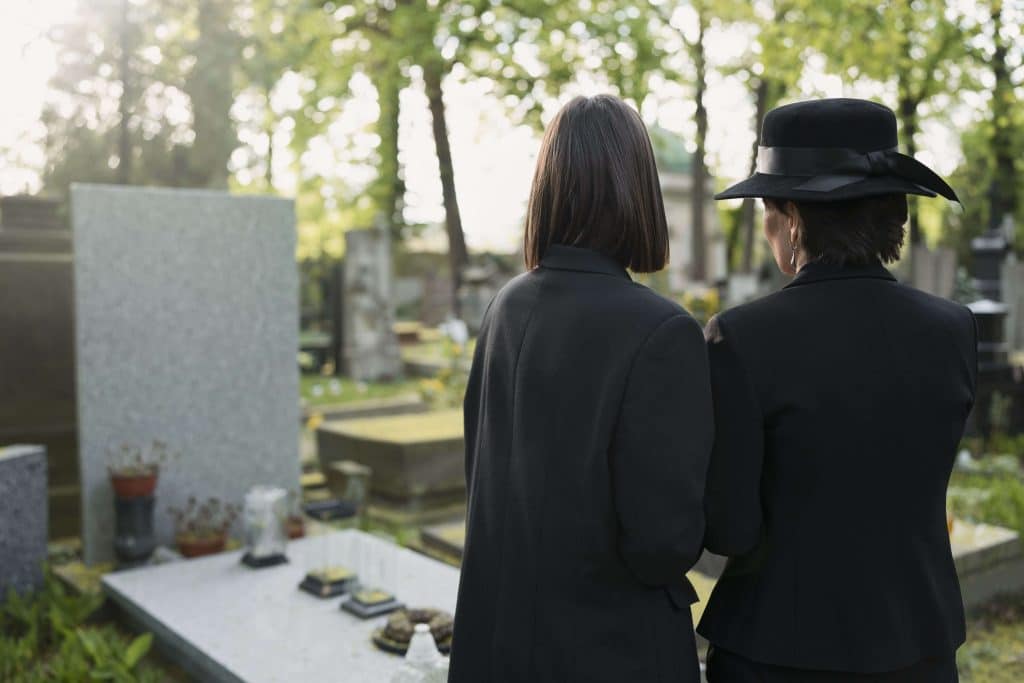 Two grieving women at a tombstone in a cemetery